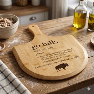 May include: A bamboo cutting board with a handle, featuring the phrase "go bills" and a definition. The board includes a buffalo silhouette and the text "Welcome to Buffalo! Go Bills!" on a wooden surface.