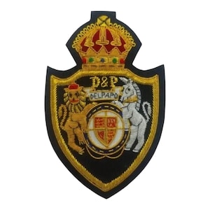 Puede incluir: Parche bordado con un diseño de escudo. El parche presenta una corona dorada, un león, un caballo y un escudo con el texto "D&P DELPAPO". El parche tiene un fondo negro con ribete dorado.