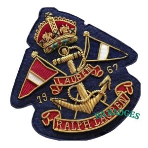 以下が含まれることがあります： 金色の錨、旗、王冠が刺繍されたネイビーブルーのパッチ。パッチには、赤色の「LAUREN」と「RALPH LAUREN」の文字と、「19」と「67」の数字が含まれています。