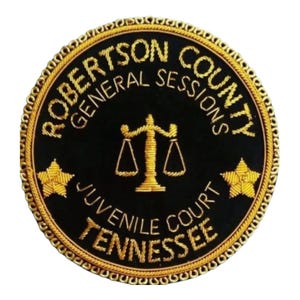 May include: A circular patch with gold embroidery on a black background. The text "ROBERTSON COUNTY GENERAL SESSIONS JUVENILE COURT TENNESSEE" is displayed. A gold scale of justice and two gold stars are also featured.