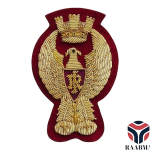May include: A maroon embroidered patch with a gold eagle design, crown, and shield. The eagle has outstretched wings, and the patch is detailed with gold thread on a maroon felt backing. The design is symmetrical and centered.
