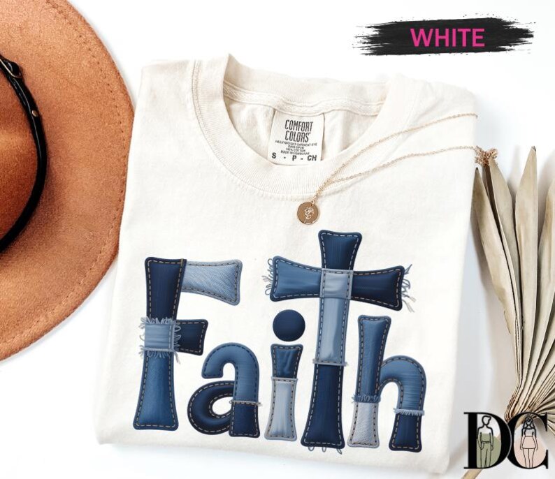 a white t-shirt with a blue cross design and the word "Faith" written on it. The t-shirt is placed on a white background, along with a brown hat and a fan.