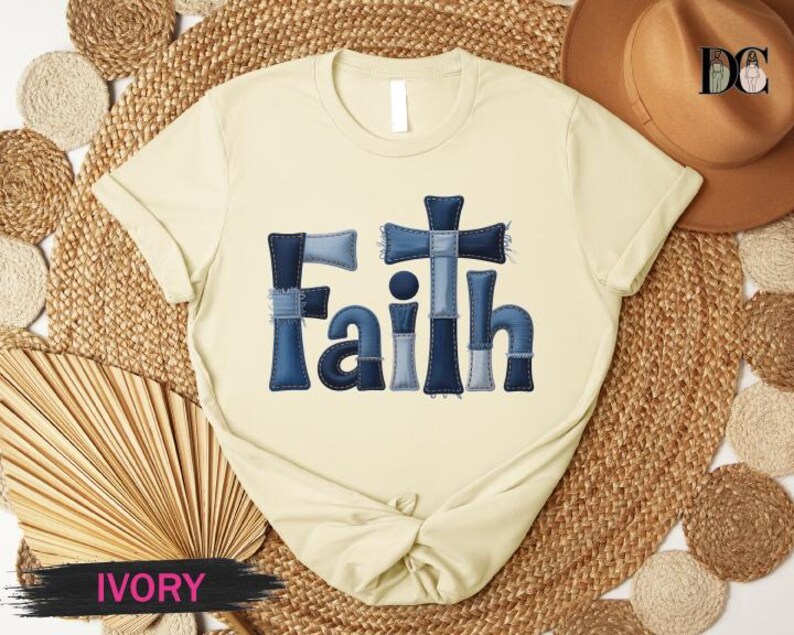 A beige t-shirt with the word "Faith" printed in blue denim-like letters, placed on a woven mat.