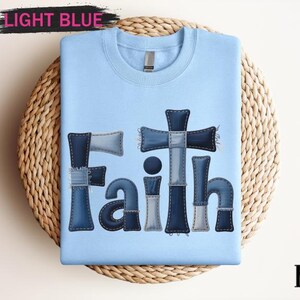 A light blue t-shirt with the word "Faith" printed in a patchwork style, made up of various fabric pieces in shades of blue and gray.