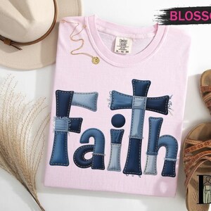 a pink t-shirt with the word "Faith" written in blue denim patches, a beige hat, a pair of brown sandals, and some dried flowers.
