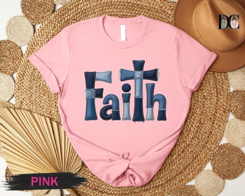 A pink t-shirt with the word "Faith" printed in blue denim jeans-like letters, placed on a woven mat.