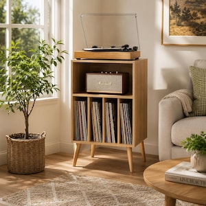 May include: A light wood record player stand featuring a top surface for a turntable, a middle shelf housing a brown Marshall speaker, and four vertical storage compartments below for vinyl records, all supported by four tapered wooden legs.