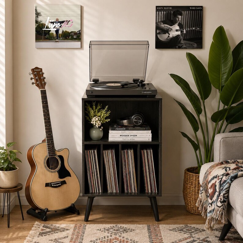 May include: A black wooden record player stand with a top surface holding a turntable, a middle shelf with books and headphones, and four lower vertical compartments filled with vinyl records, standing on four tapered legs in a room.