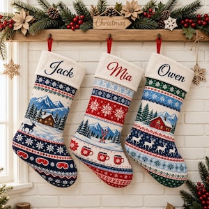 May include: Three personalized Christmas stockings with white cuffs featuring the names Jack, Mia, and Owen. The stockings display winter scenes with mountains, pine trees, deer, red cabins, mugs, and ski equipment in blue, red, and green patterns.