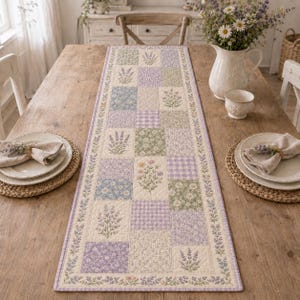 May include: A rectangular quilted table runner featuring a patchwork design of lavender, sage green, and cream squares. The fabric displays floral patterns, small sprigs of lavender, and gingham checks, finished with a lavender-colored border.
