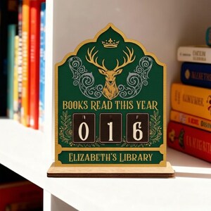 May include: A wooden desk calendar with a green background and gold detailing. The calendar reads "BOOKS READ THIS YEAR" and displays "016". A deer head and crown are at the top. The text "ELIZABETH'S LIBRARY" is at the bottom.