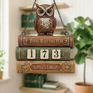 Puede incluir: Una figura decorativa de búho posada sobre tres placas apiladas con forma de libros. La placa superior dice "Books Read This Year", la del medio muestra "173" y la inferior dice "Sophia's Library". El búho y los libros son marrones y verdes.