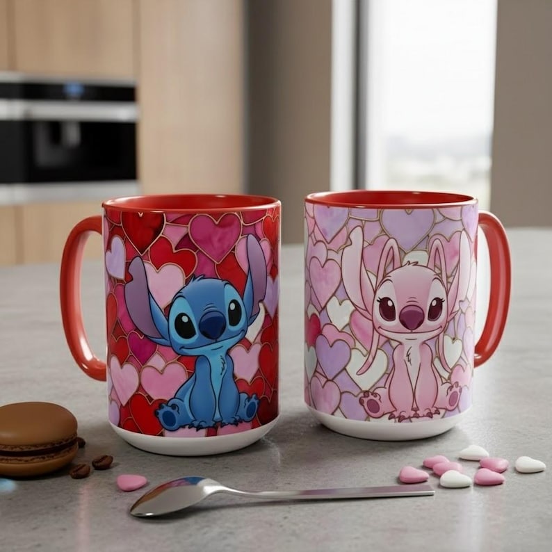 May include: Two ceramic mugs with red handles and rims. One mug features a blue cartoon character on a background of red and pink hearts. The other mug has a pink cartoon character on a background of pink and purple hearts.