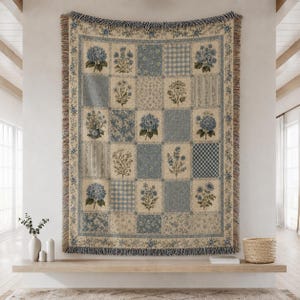 May include: A woven throw blanket featuring a patchwork design of blue and cream squares. The pattern includes various floral motifs, gingham checks, and striped textures. The blanket has a fringed edge along the top and bottom borders.
