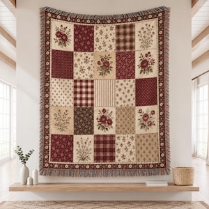 Puede incluir: Una manta tejida rectangular con un diseño de patchwork de cuadrados alternos en tonos rojo oscuro, crema y marrón. El patrón incluye motivos florales, cuadros, rayas y pequeños estampados geométricos con un borde de flecos.