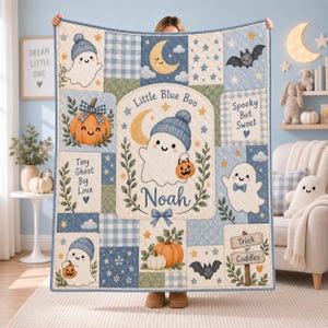 May include: A rectangular quilt featuring a patchwork design with blue, cream, and green tones. It displays illustrations of ghosts wearing blue beanies, pumpkins, bats, and stars. Text includes Little Blue Boo, Noah, Tiny Ghost Big Love, Spooky But Sweet, and Trick or Cuddles.