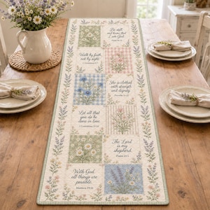 Op de afbeelding: Een rechthoekige, doorgestikte tafelloper met een patchworkontwerp van bloemenillustraties en religieuze teksten. De stof toont diverse pastelkleurige vierkanten met patronen zoals vichy-ruitjes, strepen en botanische motieven.