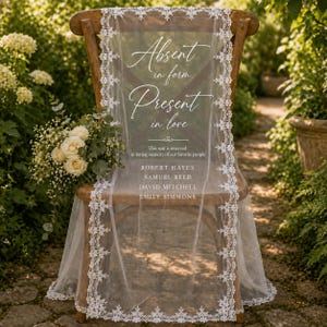 May include: A wooden cross-back chair draped with a white lace-trimmed veil featuring the text Absent in form. Present in love. This seat is reserved in loving memory of our favorite people, followed by the names Robert Hayes, Samuel Reed, David Mitchell, and Emily Simmons.
