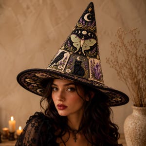 May include: A black pointed hat featuring intricate embroidery of a pale green moth, a black cat, a raven, purple crystals, and moon phases. The design includes floral accents and stars on a dark fabric base with a wide, circular brim.