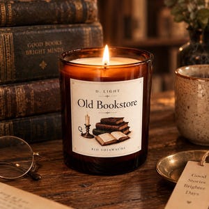 Könnte beinhalten: Eine brennende Kerze in einem braunen Glasgefäß mit einem weißen Etikett, das den Text D. LIGHT, Old Bookstore und BIO SOJAWACHS sowie eine Illustration einer Kerze im Halter und einen Bücherstapel zeigt. Die Kerze brennt mit einer warmen Flamme.