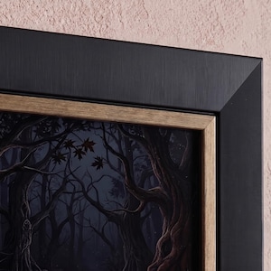 May include: A framed wall art piece featuring a dark forest scene with gnarled, textured tree trunks and deep blue shadows. The artwork is enclosed in a wide, matte black frame with a thin, light brown wood-toned inner border trim.