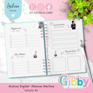 May include: Open planner with a light blue cover and silver spiral binding. The planner has sections for goals, favorite songs, and memories. The text "Archivo Digital - Planner Merlina" and "Tama&ntilde;o A5" are visible. A white pen with a crown is on the right.