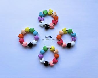 May include: Four colorful, beaded rings with various shapes, including butterflies, stars, and hearts. Each ring features a different color scheme, with a mix of rainbow hues and black and white accents. The rings are arranged on a white surface, with the text "LovElly" visible.