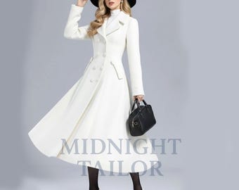 Puede incluir: Un abrigo largo blanco con diseño de doble botonadura y falda acampanada. El abrigo presenta botones grandes y un cuello clásico. Un sombrero y un bolso negros completan el look. El texto "MIDNIGHT TAILOR" es visible en la parte inferior del abrigo.