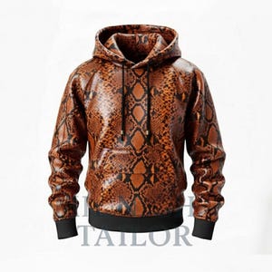 Pode incluir: Moletom marrom e preto com estampa de pele de cobra, com capuz com cordão e bolso canguru. Os punhos e a bainha são pretos. A palavra "TAILOR" é visível na parte inferior da imagem.