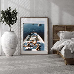 May include: A framed print depicts a yacht on the ocean with people sunbathing on the deck. The yacht has a blue deck with a white jacuzzi. The ocean is a deep blue, and other boats are visible in the distance.