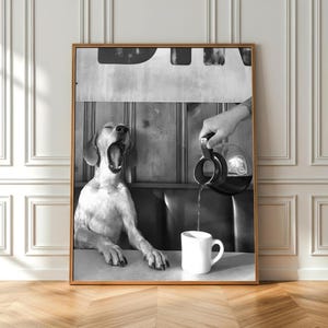 May include: Black and white framed print featuring a yawning dog seated at a table. A hand pours liquid from a carafe into a white mug. The background includes a wooden wall and a diner-style booth.