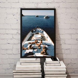 May include: A framed print depicting a yacht with people sunbathing on the deck. The yacht is on the water with other boats in the distance. The deck has a blue cover and a small jacuzzi. The print is displayed on a stack of books.