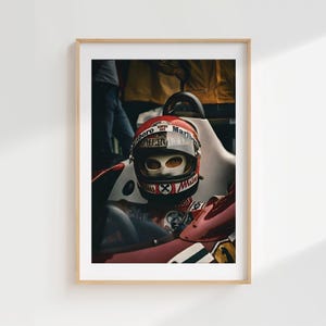 May include: Framed print of a vintage Formula 1 race car driver in a red and white helmet with the Marlboro logo. The driver is seated in a red race car. The image is set in a wooden frame.