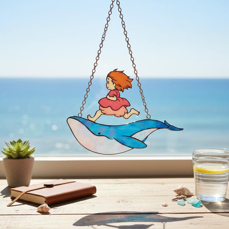 May include: A stained glass suncatcher depicting a girl in a pink dress running on a blue whale. The whale is suspended by a chain, with the sea and sky in the background. This decorative item is designed to catch the sunlight.