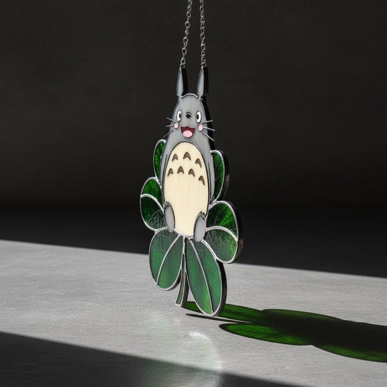 Peut inclure: Pendentif Totoro gris et cr&egrave;me, orn&eacute; de feuilles vertes. Le pendentif est suspendu &agrave; une cha&icirc;ne argent&eacute;e. Le personnage de Totoro souriant est entour&eacute; de feuilles vertes.