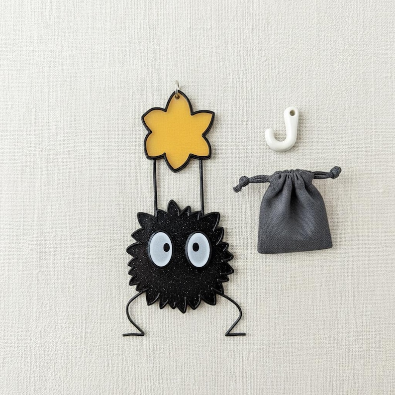Peut inclure: Un personnage noir et jaune fantaisiste avec de grands yeux blancs, tenant une fleur jaune. Un petit sac gris &agrave; cordon et un crochet blanc sont &eacute;galement pr&eacute;sents. Le personnage a une apparence textur&eacute;e et &eacute;pineuse, et la fleur est soulign&eacute;e en noir.