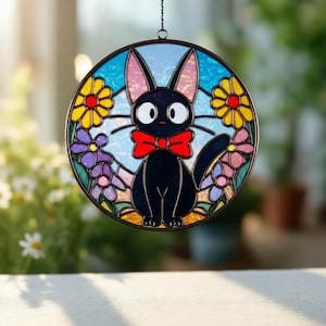 May include: A round stained glass window decoration featuring a black cat with a red bow tie, surrounded by colorful flowers. The cat has large white eyes and pink-lined ears. The background is blue with a light sky effect.