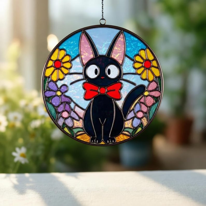 May include: A round stained glass window decoration featuring a black cat with a red bow tie, surrounded by colorful flowers. The cat has large white eyes and pink-lined ears. The background is blue with a light sky effect.