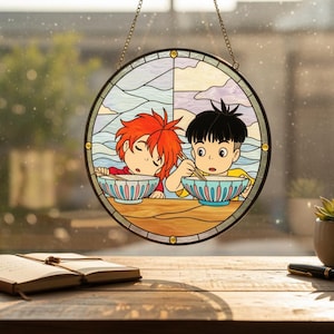 May include: A circular stained glass window panel depicting two anime-style figures enjoying ramen. The artwork uses blue, yellow, and red hues, with a black border and a hanging chain. The panel is displayed in front of a window.