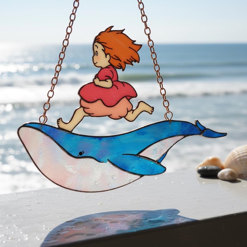May include: Stained glass artwork showing a girl in a red dress running on a blue whale, hanging by copper chains. The whale has blue and white details. The girl has orange hair. The background features the sea.