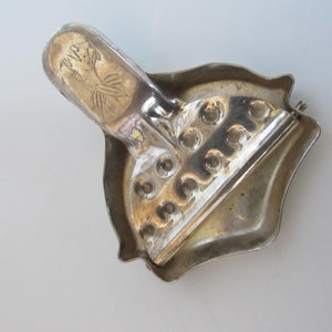Op de afbeelding: Zilverkleurige metalen broche met een decoratief ontwerp. De broche heeft een scharnierende sluiting en een decoratief ontwerp aan de achterkant.