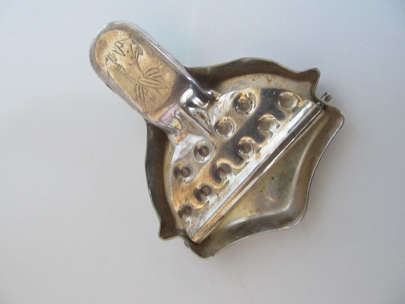 Op de afbeelding: Zilverkleurige metalen broche met een decoratief ontwerp. De broche heeft een scharnierende sluiting en een decoratief ontwerp aan de achterkant.