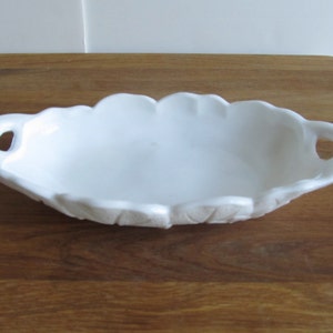 May include: White ceramic serving dish with two handles. The dish has a scalloped edge and a textured design.