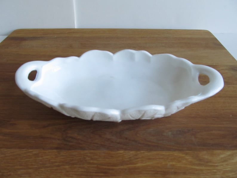 May include: White ceramic serving dish with two handles. The dish has a scalloped edge and a textured design.