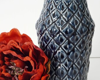 May include: A dark blue ceramic vase with a geometric pattern. The vase is textured and has a glossy finish.