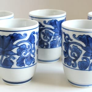 May include: Set of five white ceramic teacups with blue floral designs. The cups have a simple, elegant design.
