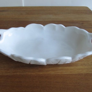 May include: White ceramic serving dish with two handles. The dish has a scalloped edge and a smooth, glossy finish.