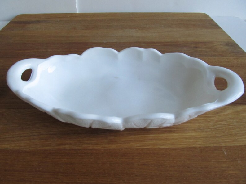 May include: White ceramic serving dish with two handles. The dish has a scalloped edge and a smooth, glossy finish.