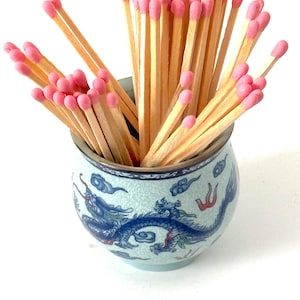 May include: A blue and white ceramic jar with a dragon design, filled with wooden matches with pink tips.