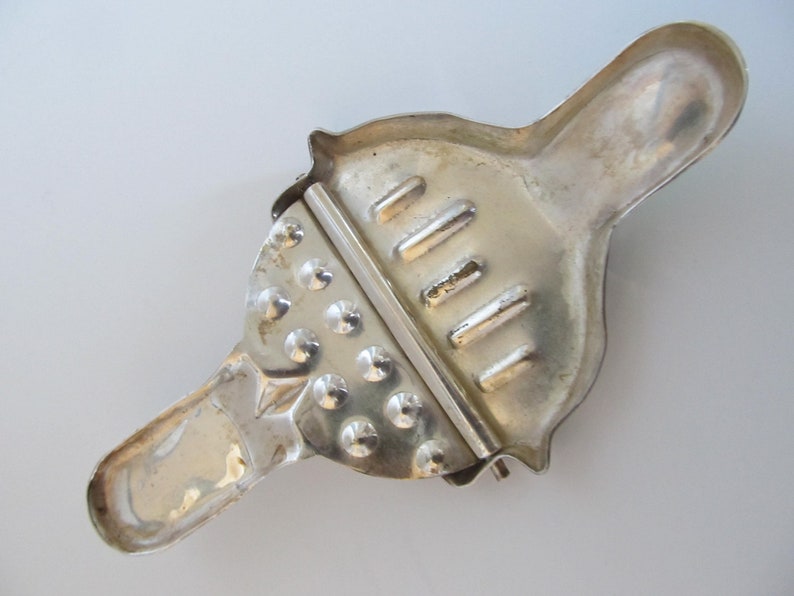Op de afbeelding: Zilveren metalen citruspers met een handvat en een getextureerd oppervlak. De citruspers heeft een hendel die op de citrusvrucht drukt.